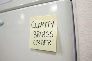 Yellow sticky note with Clarity Brings Order message on a white surface