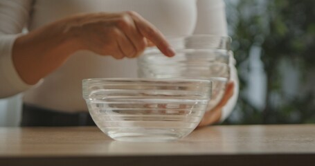 Close up of a woman hand arranging a stack of transparent glass bowls, showcasing home organization.