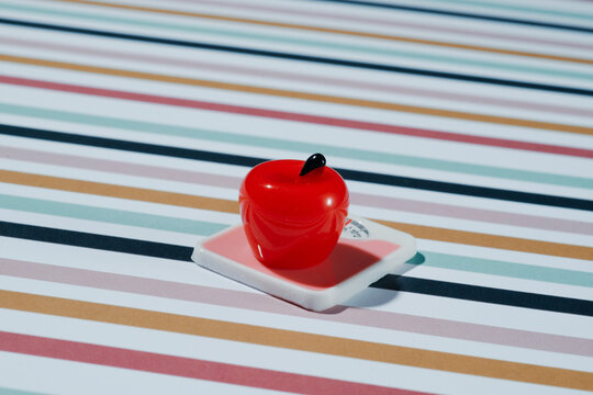 Shiny red toy apple on small white scale with striped pop art background