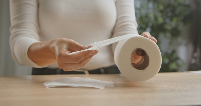 Close up of woman hands holding a toilet paper roll above a wooden table, emphasizing hygiene and daily essentials.