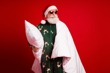 Santa in cozy pajama cape holds pillow smiles under red background for Christmas fun and festive...