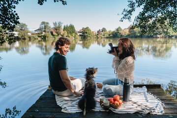Couple relaxing with dog at lakeside picnic enjoying photography outdoors