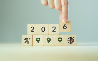 2026 goal achievement path, business planning concept. Wooden blocks with 2026, professional businessman, location icons and a target symbol, representing planning, milestones and achieving goals.