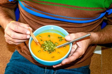Hand holding bowl of homemade pumpkin soup with seeds close up