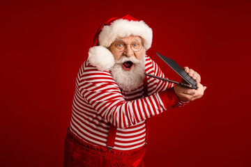 Santa Claus character in striped shirt and red suspenders bursts with astonishment as he holds a...