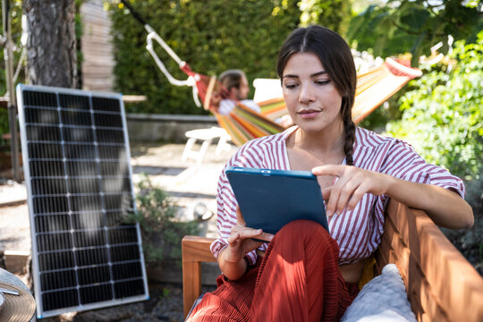 Smiling woman using tablet PC near solar panel in back yard