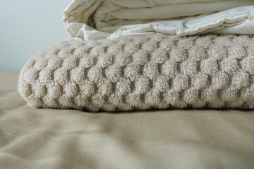 A stack of beige bed linens on the bed. A beautiful, warm beige blanket.
