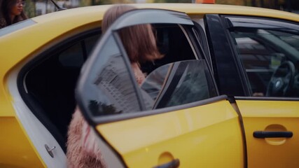 Stylish women getting into a yellow taxi cab after calling for a ride on a city street