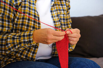 Close-up of woman&rsquo;s hands knitting bright red fabric. Concept of hobby, coziness and handmade creativity.