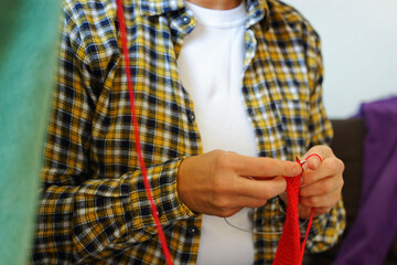 Woman in checkered shirt knitting red fabric with needles, top view. Cozy and creative atmosphere.