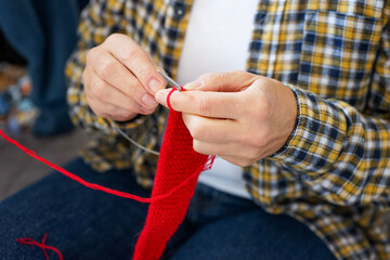 Woman in checkered shirt knitting red fabric with needles, top view. Cozy and creative atmosphere.