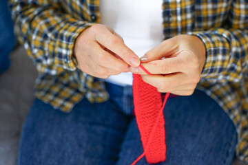 Close-up of woman&rsquo;s hands knitting bright red fabric. Concept of hobby, coziness and handmade creativity.