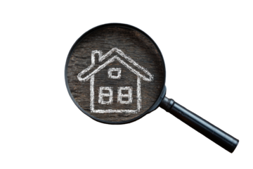 Magnifying glass focuses on a chalk drawing of a house on a dark, wooden surface