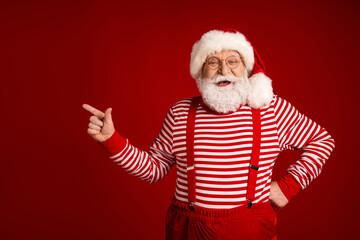 Festive Santa Claus wearing a striped shirt and suspenders points playfully against a red background