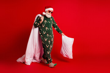 Santa in a festive green pajama with reindeer pattern and white cape stands against a red...