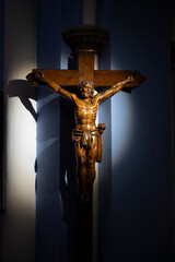 A wooden crucifix stands out against the blue wall of Basilique Notre-Dame-de-Buglose in Saint-Vincent-de-Paul. The light highlights the details of the sculpture, creating a serene atmosphere.