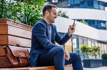 Smiling businessman checking phone outside corporate office