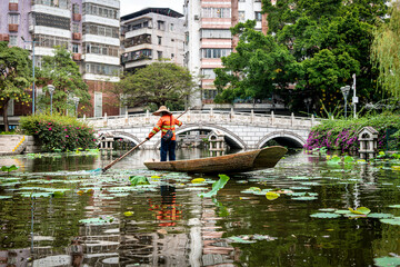 A person paddles a wooden boat amid tranquil lotus waters