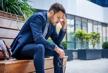 Unemployment problem. Fired depressed businessman sitting in front of corporation. Business concept
