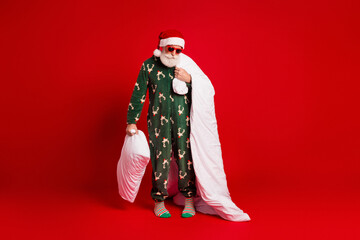 Festive Santa in a green Christmas onesie holding a white pillow with red backdrop and playful...