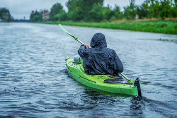 Man paddling a canoe on a calm river in raincoat. The face is not recognizable. Sport and recreation