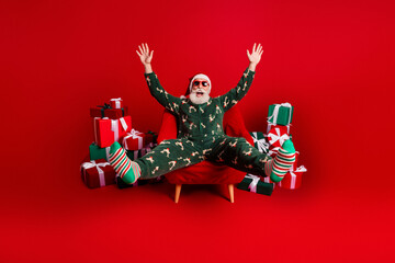 Santa in festive pajama suit celebrates christmas morning while lounging in a bright red studio...