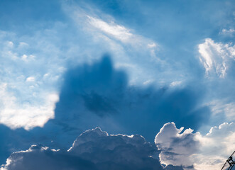 Dramatic sunbeams breaking through white cumulus clouds in deep blue sky creating crepuscular rays and divine light