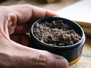 Black and Gold Herb Grinder with Ground Cannabis on Wooden Table Surface