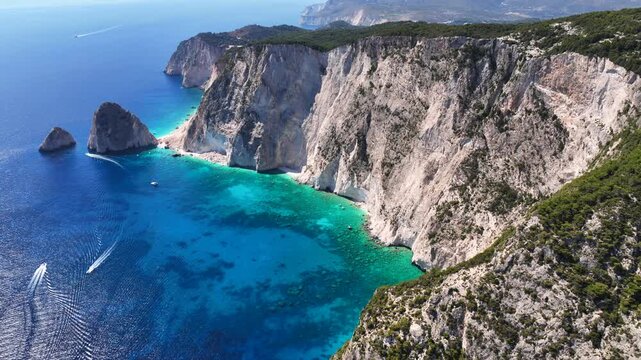 Aerial drone cinematic video of paradise tropical destination island with volcanic caves and white cliffs visited by yachts and sail boats forming a blue lagoon with turquoise crystal clear waters