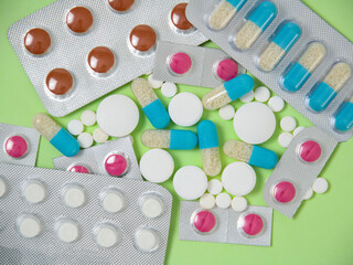 Multi-colored medical tablets, capsules and vitamins highlighted on a green background. 