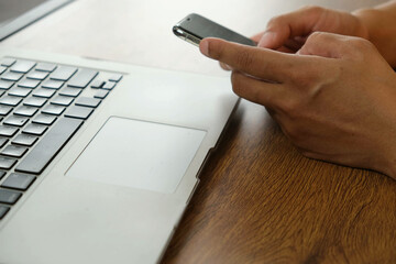 Person using smartphone near laptop on wooden desk, mobile transaction technology, digital communication and online connectivity concept