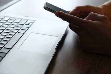 Person using smartphone near laptop on wooden desk, mobile transaction technology concept