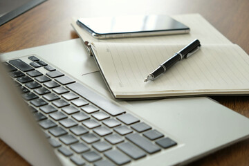 Laptop keyboard, notebook, pen, and smartphone on wooden desk showing business planning and learning setup