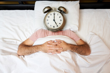Man with alarm clock instead of head lying in bed. Morning concept