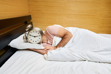 Man with alarm clock instead of head sleeping in bed. Morning concept