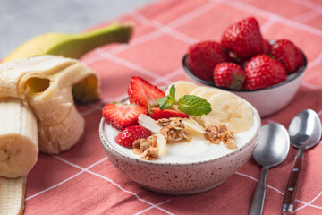 Yogurt bowl with muesli, banana and strawberries. Healthy diet fitness meal for weight loss and wellbeing