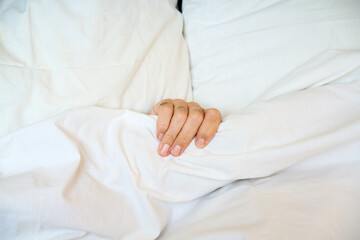 Close-up of human hand gripping a white blanket on soft bed