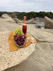 Fototapeta premium A bottle of wine with a bunch of grapes on a sandy beach, captured in soft natural light. Summery coastal mood, relaxed vacation atmosphere, elegant still life outdoors. 