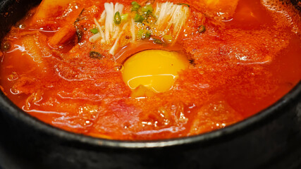 Spicy red soup with raw egg yolk and mushrooms in black bowl, warm and flavorful meal