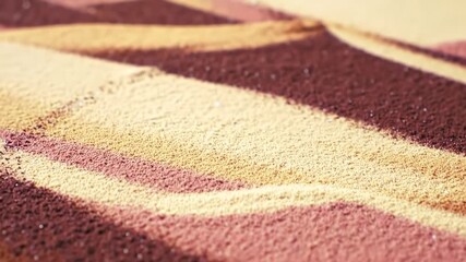 Closeup of a paintbrush creating a vibrant sand painting with intricate patterns and textures emerging from the colorful grains showcasing the delicate artistry and creative process in a serene setti.
