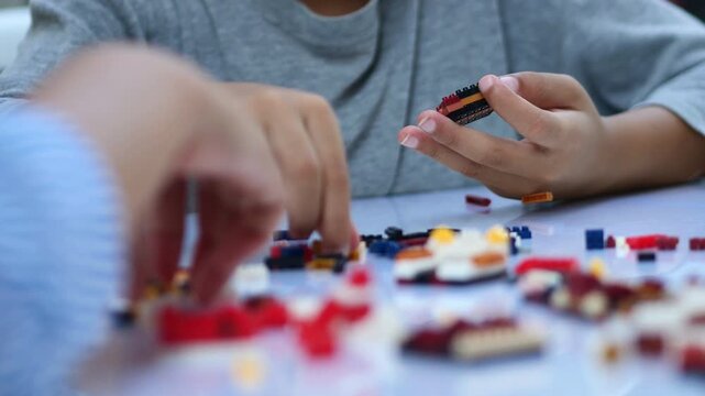 Children hands play with colorful blocks on white table.