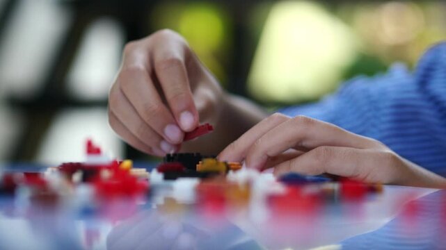 Children hands play with colorful lego blocks on white table.
