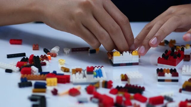 Children hands play with colorful blocks on white table.