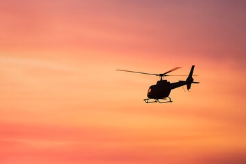 Fototapeta premium A silhouette of a helicopter against a stunning sunset paints the sky with hues of orange and pink, embodying adventure and tranquility. Perfect for travel inspiration.