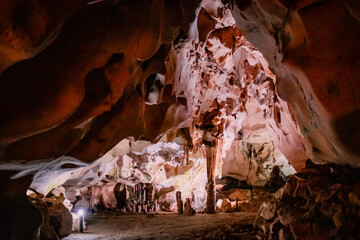 Beautiful view inside Orlova Chuka Cave in Bulgaria, showcasing impressive stalactites and stalagmites illuminated by warm artificial light. The natural rock formations create a stunning abstract patt