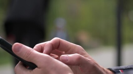 close-up view male hands holding modern smartphone while typing message and scrolling through social media feed with beautiful green blurred background park.