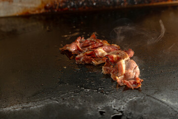 crispy bacon cooking on hot flat top griddle with steam rising