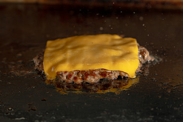 A juicy hamburger patties layered with melted cheddar cheese searing on a hot griddle