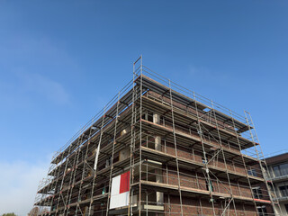 Construction site featuring a partially completed building surrounded by scaffolding under a clear blue sky, showcasing the progress of modern architecture and urban development