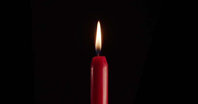A single red candle burning. Isolated candle burning with dark background. Red paraffin candle with yellow shades burns on a black background. Background or illustration of remembrance or celebration.